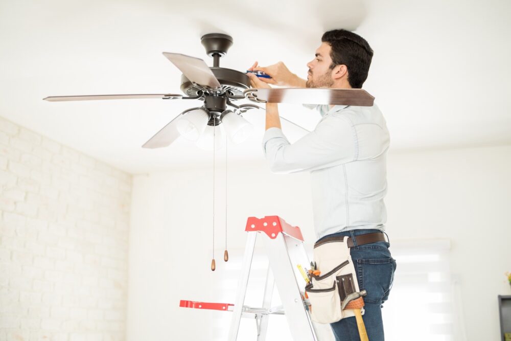 Man installing ceiling fan in home to save energy on air conditioning