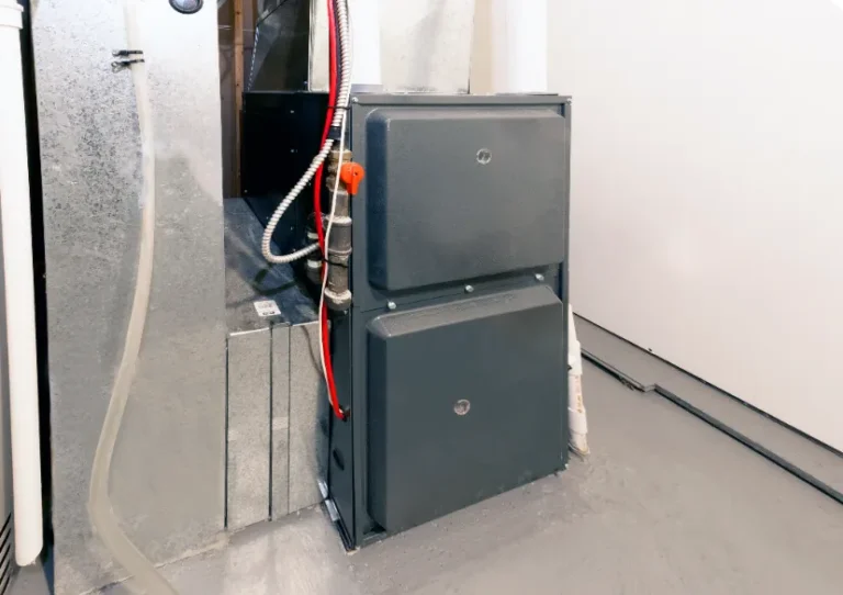 A residential furnace unit with metal ductwork installed in a clean basement or utility room with a gray floor.