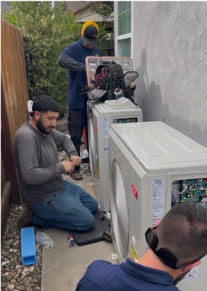 Three workers install and service outdoor HVAC units next to a building, using tools and equipment on a concrete walkway. Ask about available financing to make your new system more affordable.
